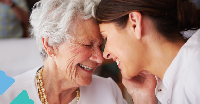 Elderly woman and younger woman smiling warmly, touching foreheads, sharing a tender moment.