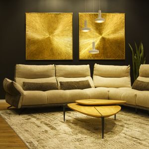 Modern living room with a beige sectional sofa, wooden coffee table, textured rug, gold abstract wall art, and pendant lighting.