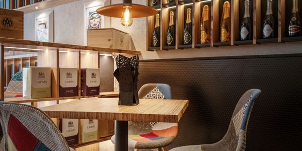 Cozy wine cellar with wooden shelves filled with bottles, illuminated by warm lighting. Two colorful, cushioned chairs at a wooden table.