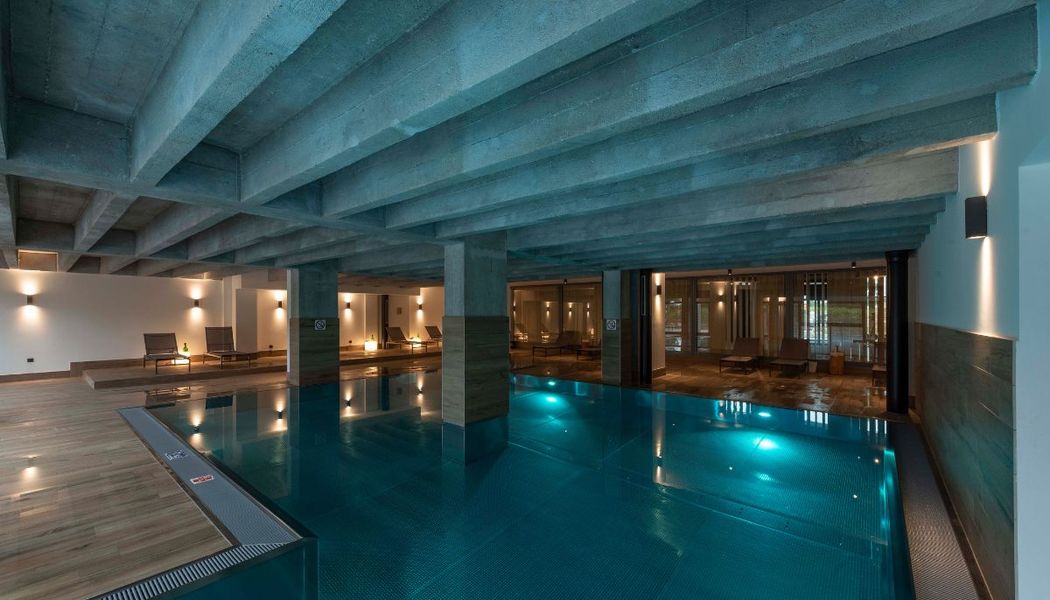 Indoor Pool mit moderner Beton-Ästhetik und SLV Wandleuchten.
