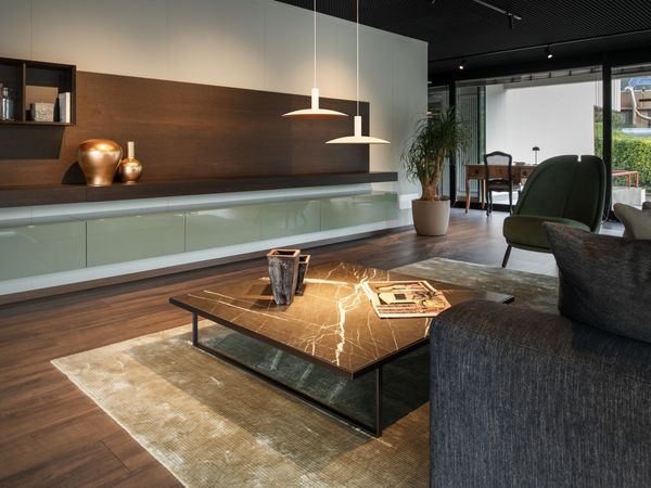Modern living room with wooden floors, sleek furnishings, a marble coffee table, pendant lights, and large windows overlooking a garden.