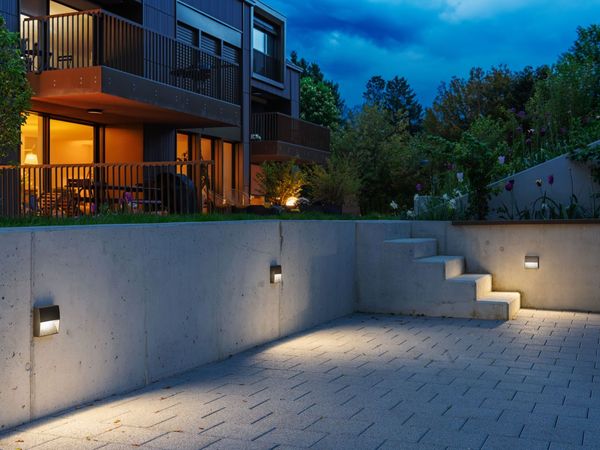 Beleuchtete Außentreppe und Gartenmauer mit quadratischen Wandleuchten bei Dämmerung