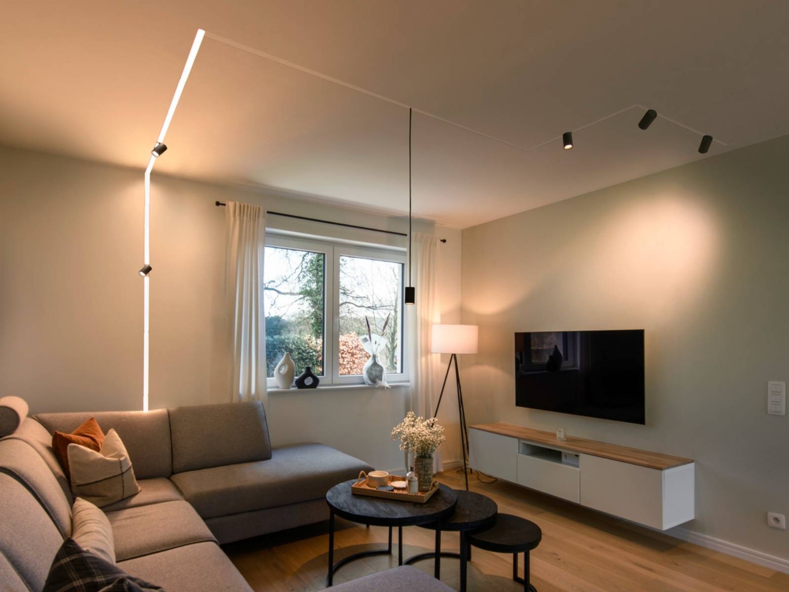 Modern eingerichtetes Wohnzimmer mit einem stilvollen 48V-Schienensystem an der Wand und Decke sowie minimalistischen Pendelleuchten und Spots.