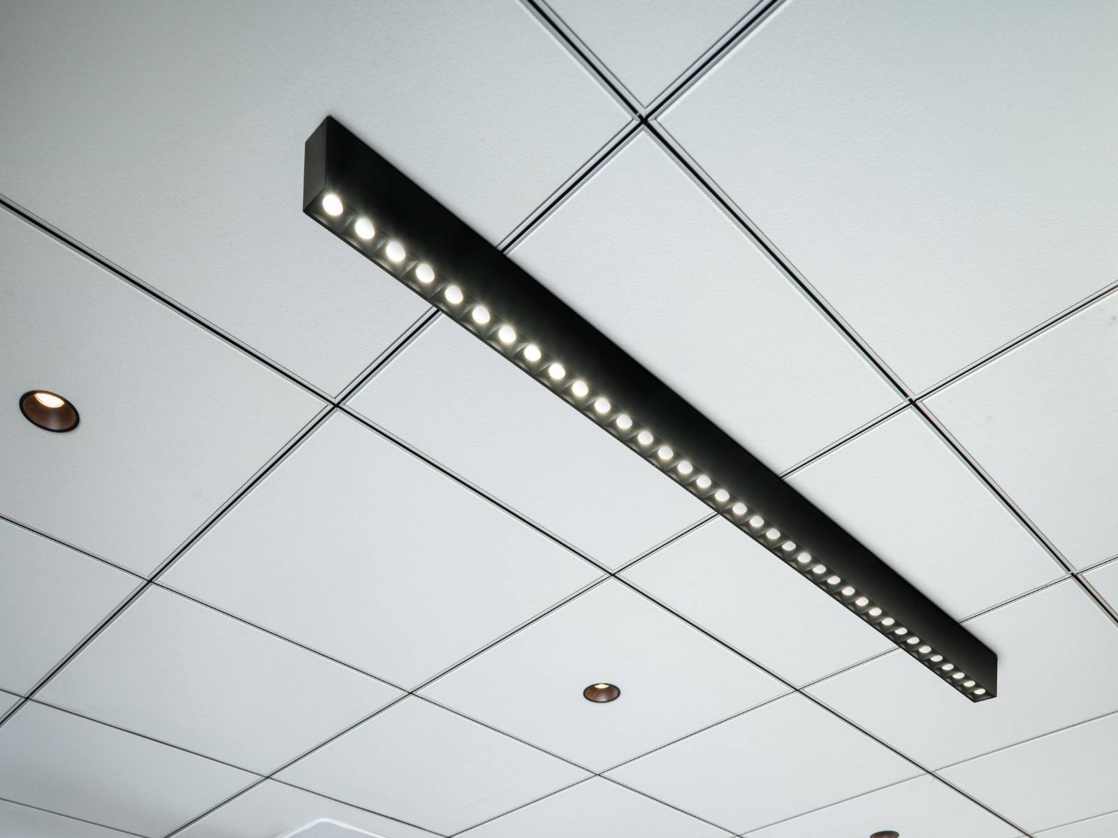 Decke mit einem Raster aus weißen Fliesen, mit GLENOS® PRO und mehreren Einbauleuchten.