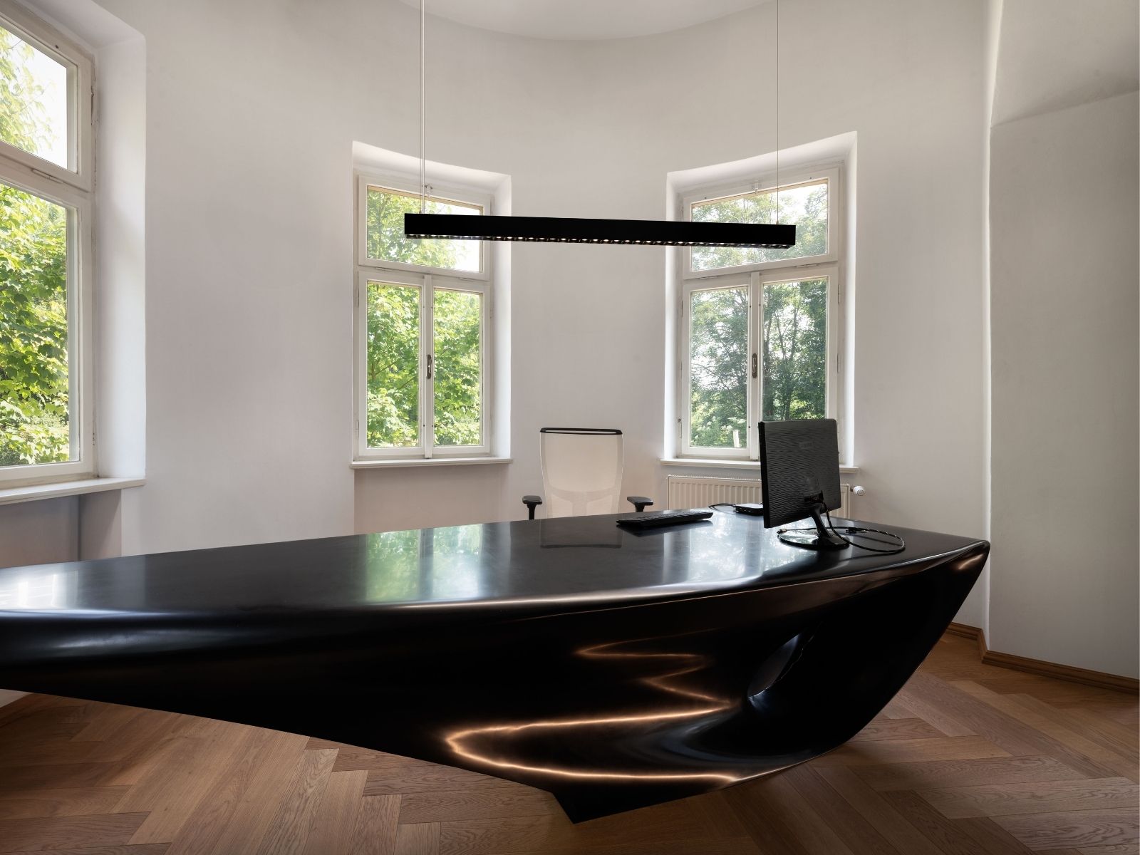 Futuristisches Büro mit einem geschwungenen, schwarzen Hochglanz-Schreibtisch und einer schlanken, linearen LED-Pendelleuchte darüber.