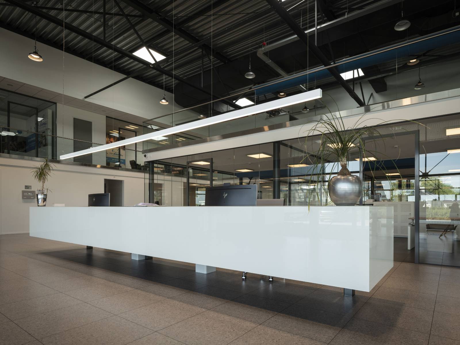Lange, weiße Empfangstheke in einer modernen Halle mit industrieller Deckenstruktur und einer schmalen LED-Lichtlinie