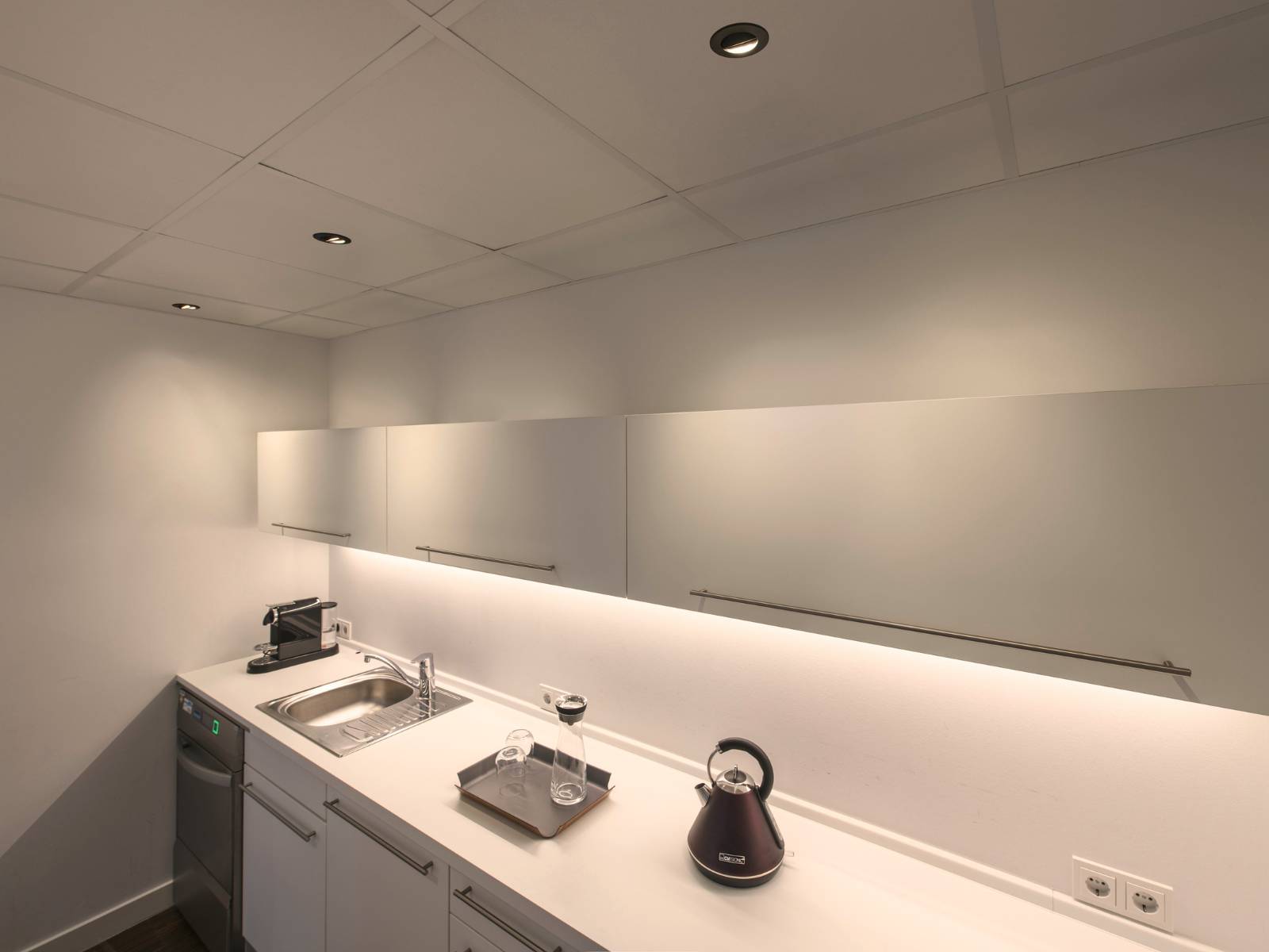Drei schwarze runde SLV Universal Downlights in einer weißen Systemdecke über einer minimalistischen weißen Küchenzeile
