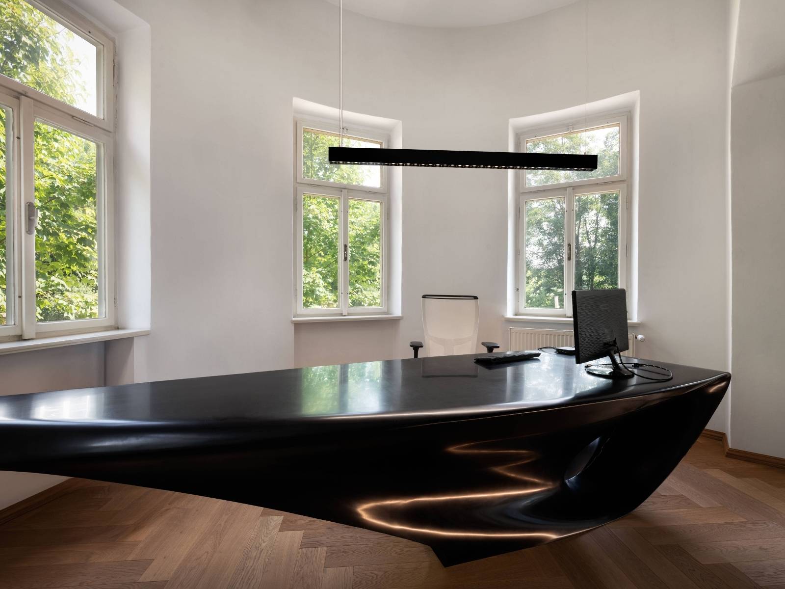 Futuristisches Büro mit einem geschwungenen, schwarzen Hochglanz-Schreibtisch und einer schlanken, linearen LED-Pendelleuchte darüber.