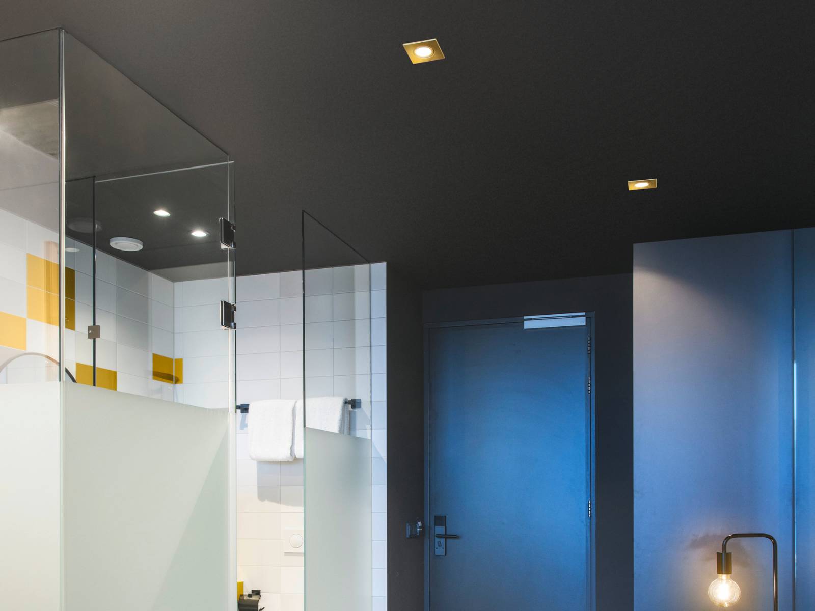 Quadratische goldfarbene Einbauleuchten in einer dunklen Decke schaffen eine edle Lichtatmosphäre in einem modern gestalteten Badezimmer
