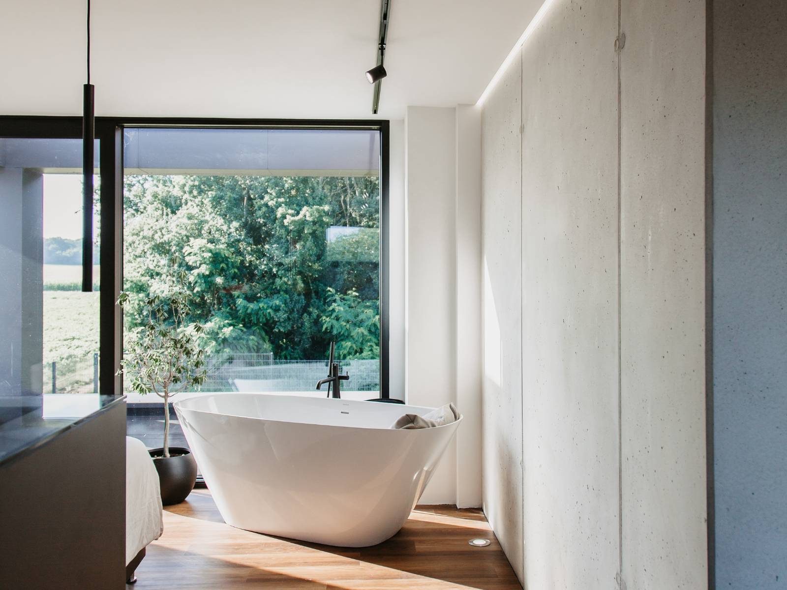 Moderna kopalnica s samostoječo belo kadjo, velikim oknom s pogledom na zelenje in minimalističnim pohištvom.