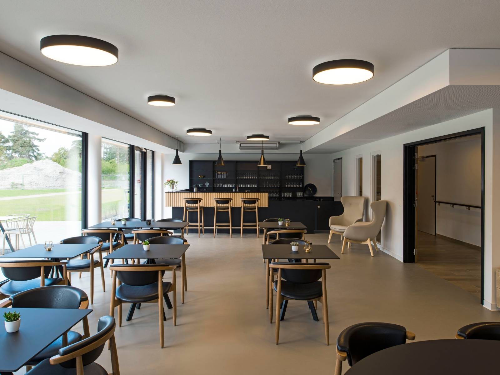 Modernes Café oder Restaurant mit mehreren großen, runden, flachen LED-Deckenleuchten in Schwarz für eine gleichmäßige Raumbeleuchtung.