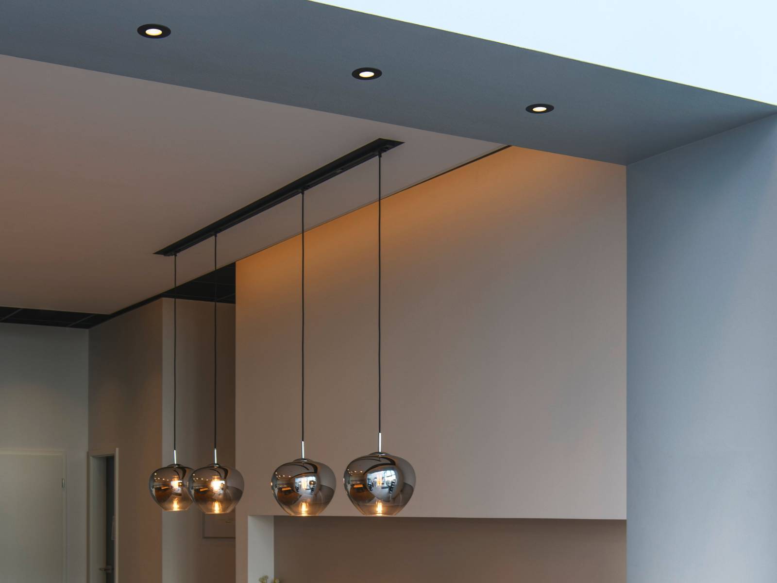 Eine Reihe von runden schwarzen Downlights in einer modernen Deckenkonstruktion oberhalb von dekorativen Glas-Pendelleuchten