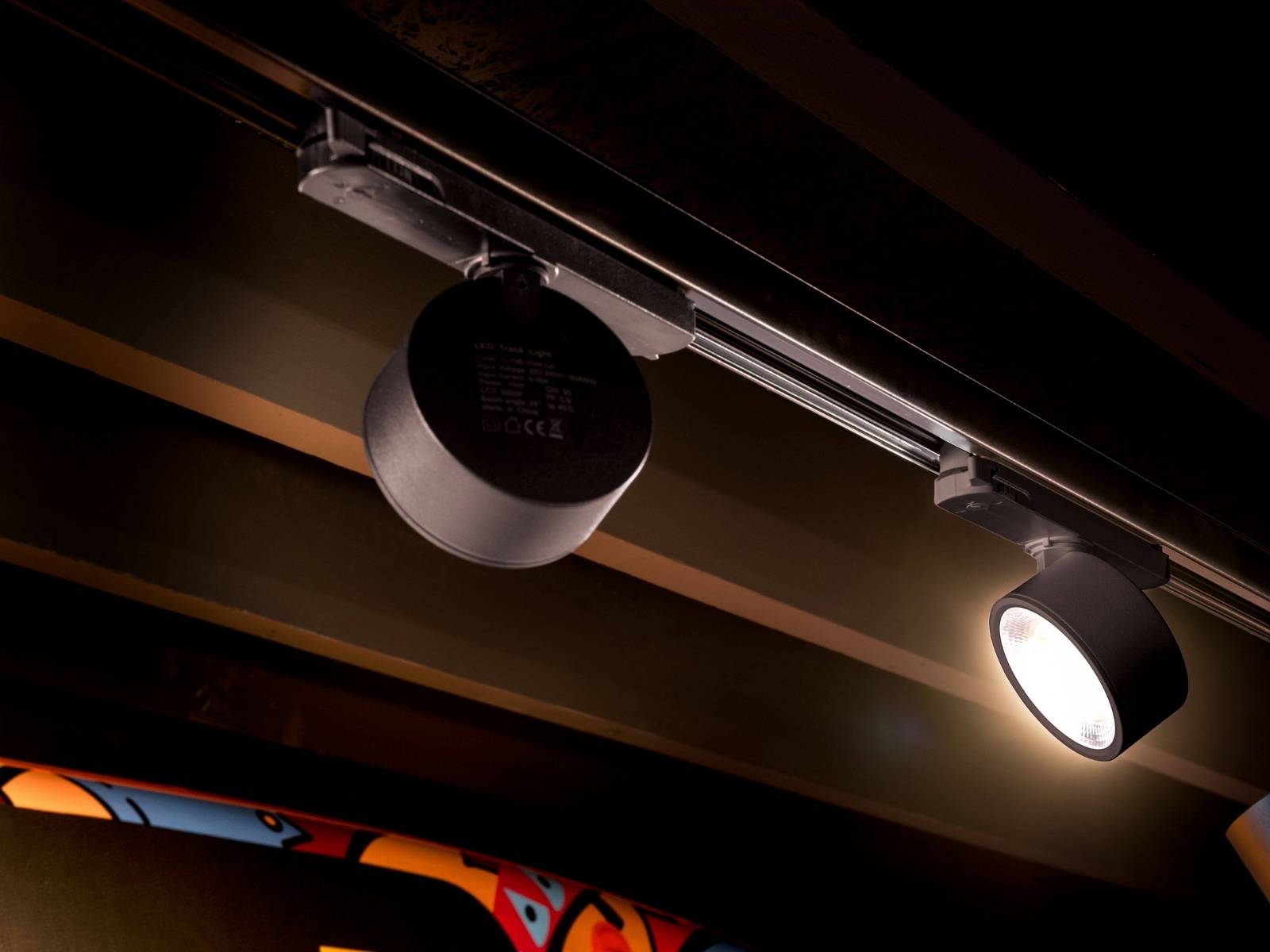 Zwei zylindrische, schwarze LED-Strahler an einer Stromschiene in einer stimmungsvoll beleuchteten Gastronomie- oder Bar-Umgebung.
