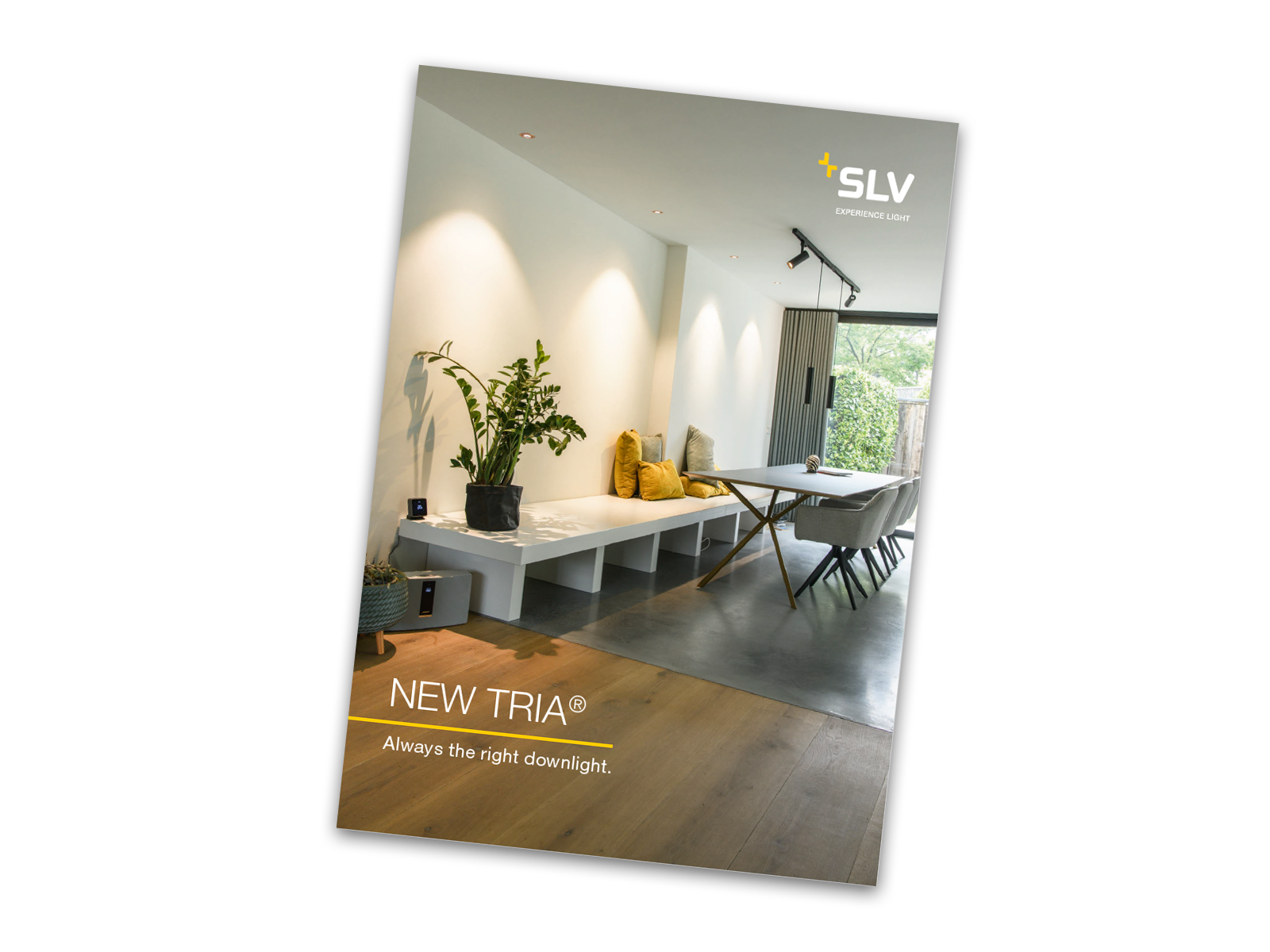 Cover der NEW TRIA® Broschüre: Moderner, minimalistischer Wohnraum mit einem langen Tisch, einer gepolsterten Bank und Pflanzen; mit dem Schriftzug „NEW TRIA®“ und dem SLV-Firmenlogo in der Ecke.