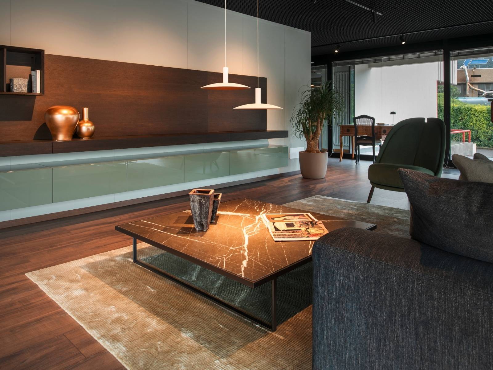 Elegantes Wohnzimmer mit dunklem Echtholzboden, großem Couchtisch und zwei flachen, weißen Designer-Pendelleuchten über der Sitzecke.