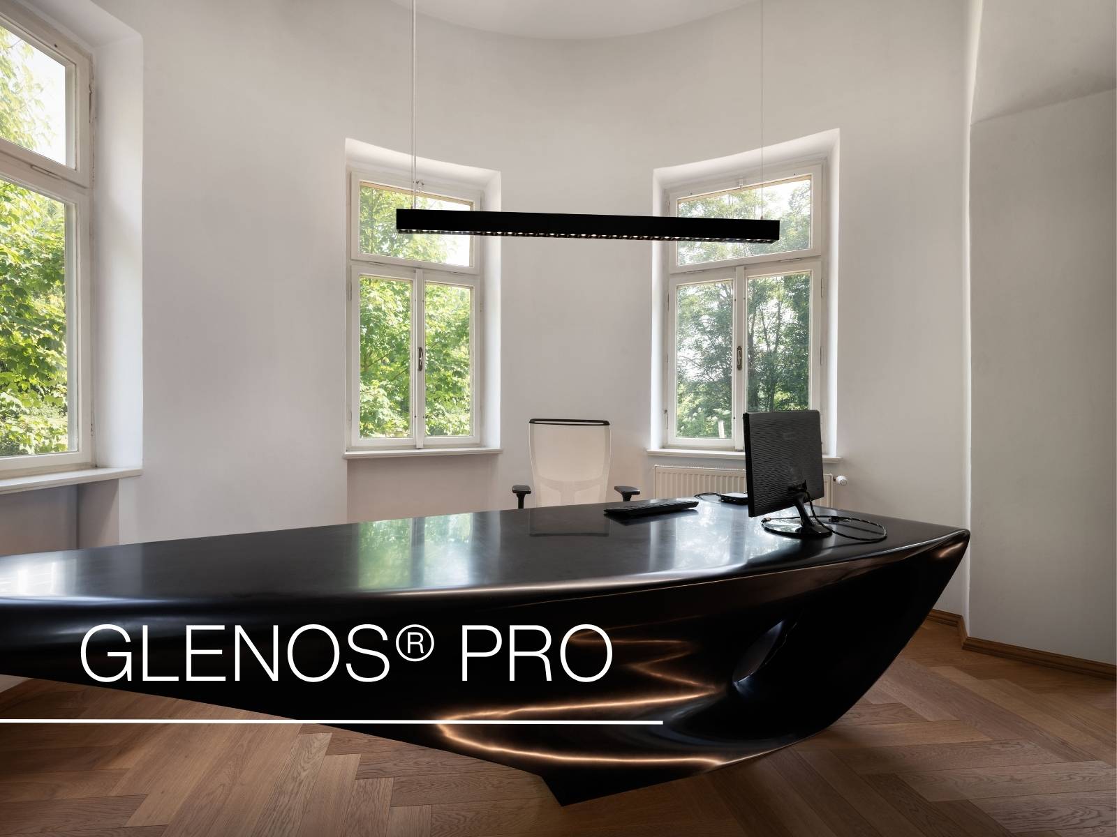 Modernes Büro mit einem eleganten schwarzen Schreibtisch, einem Computer, einem weißen Stuhl und großen Fenstern, durch die man grüne Bäume sieht. Der Text lautet „GLENOS® PRO“.