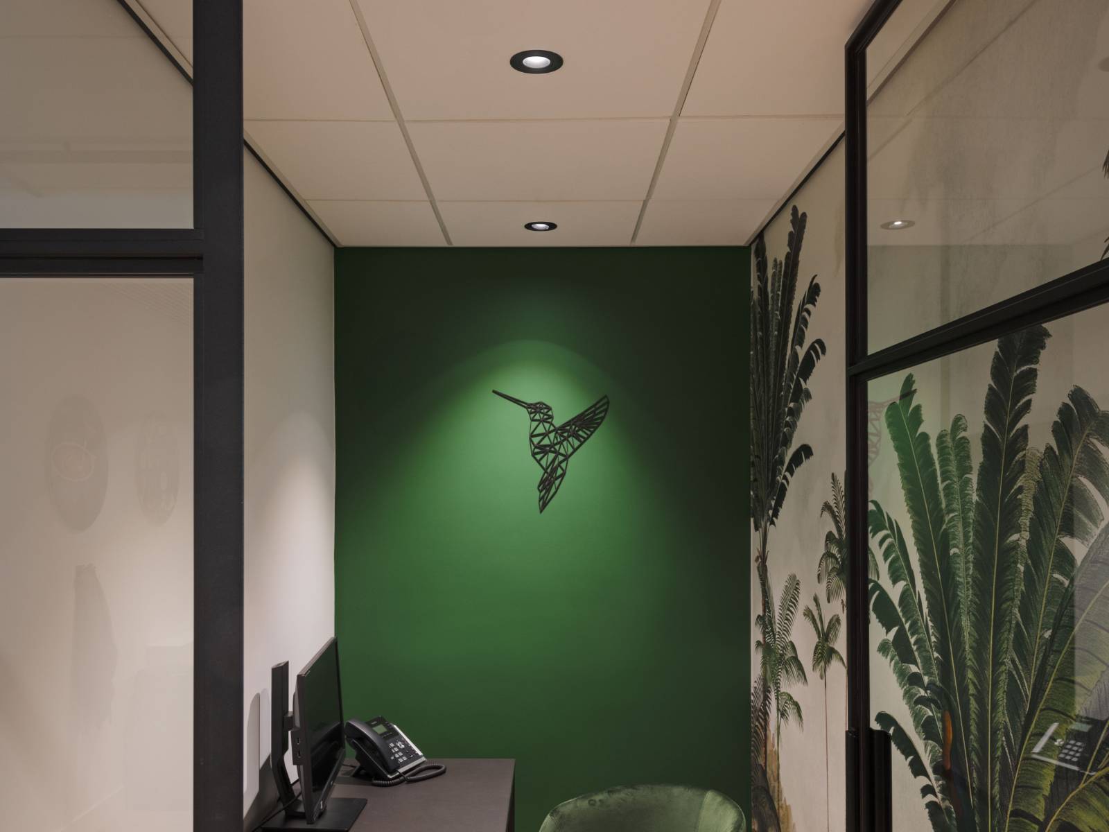 Runde schwarze SLV Universal Downlights in einer weißen Rasterdecke beleuchten einen modernen Bürobereich mit einer grünen Akzentwand und Wandkunst