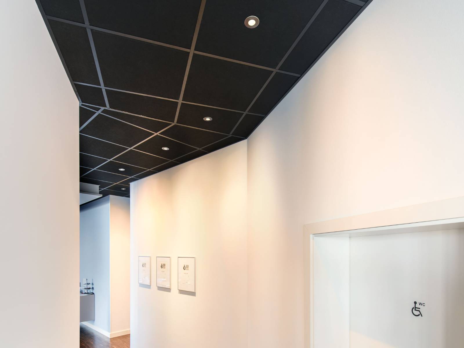 Mehrere runde SLV Universal Downlights in einer dunklen Rasterdecke sorgen für eine helle und gleichmäßige Ausleuchtung eines weißen Flurs