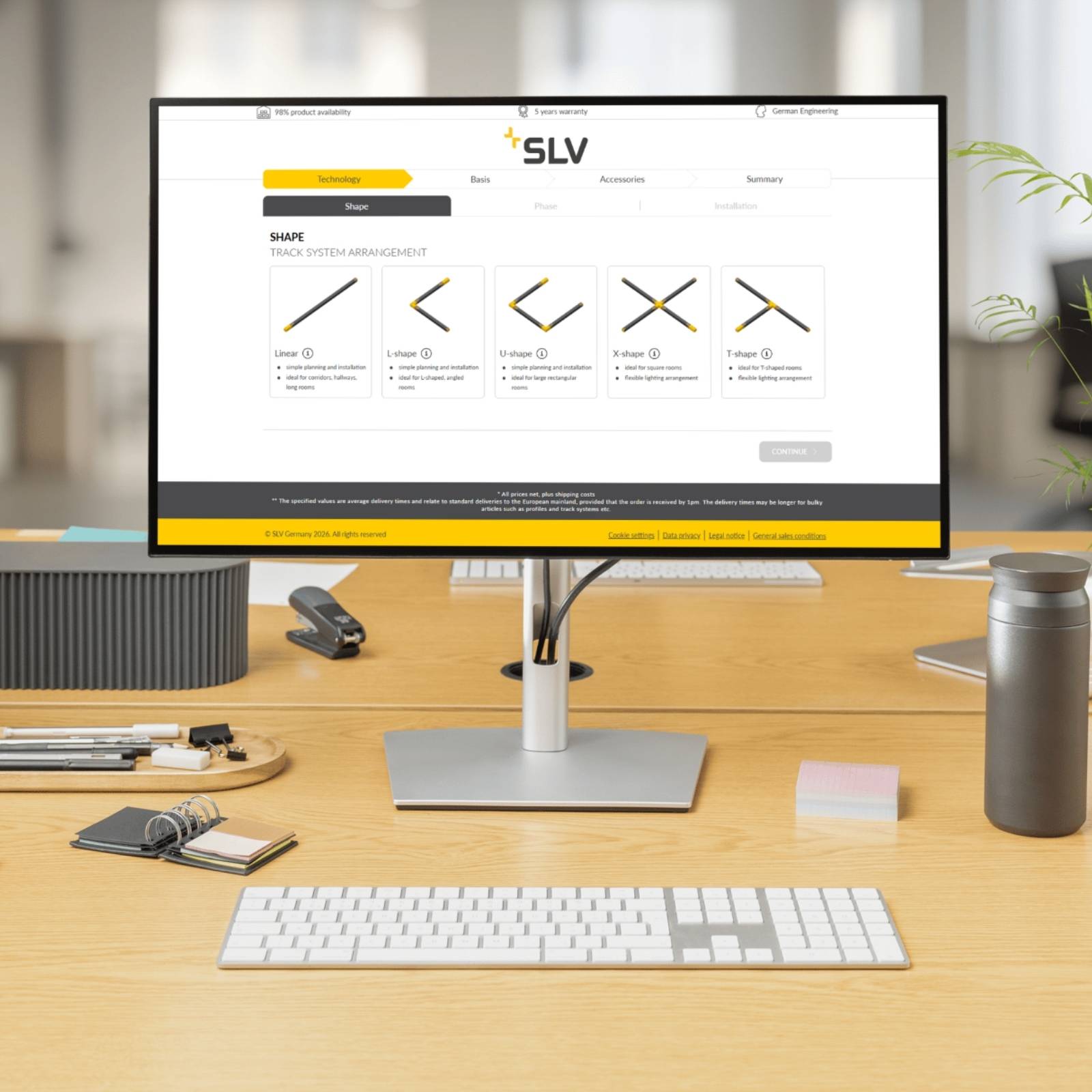 Ein auf einem Schreibtisch stehender Computermonitor zeigt das digitale SLV Konfigurations-Tool für Stromschienensysteme mit verschiedenen Anordnungsmöglichkeiten wie Linear, L-Shape, U-shape, X-shape und T-shape.