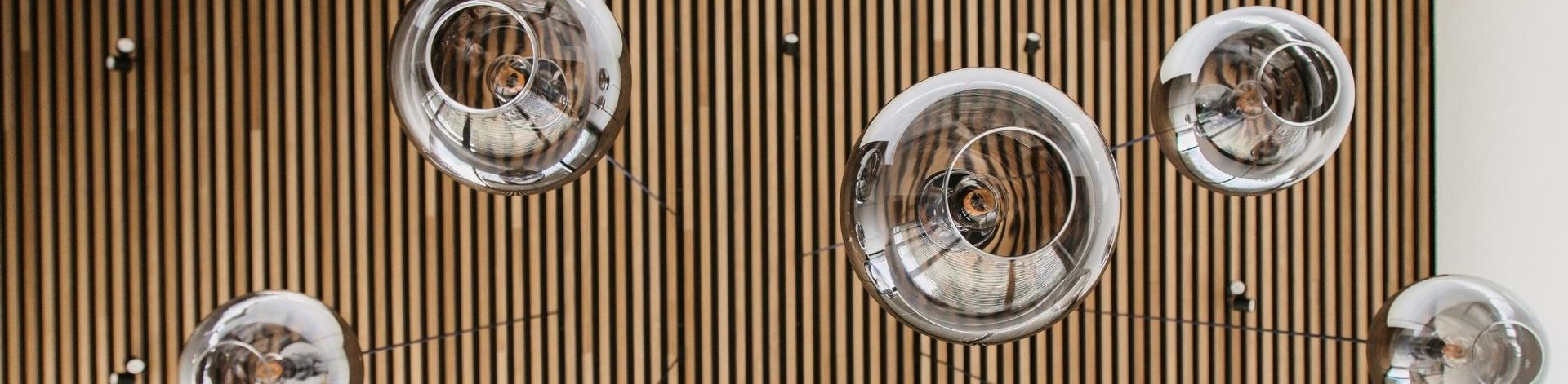 Fünf PANTILO Pendelleuchten mit Schirm aus Rauchglas, die von einer Decke aus Holzpanelen hängen, perspektivisch von unten betrachtet.