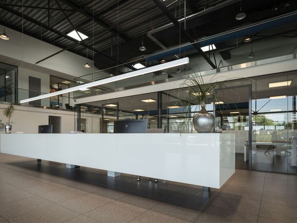 Lange, weiße Empfangstheke in einer modernen Halle mit industrieller Deckenstruktur und einer schmalen LED-Lichtlinie
