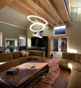Geräumiges Wohnzimmer mit braunen Sofas, einem Couchtisch aus Holz, ONE FLAT triple und großen Fenstern, die Tageslicht hereinlassen.