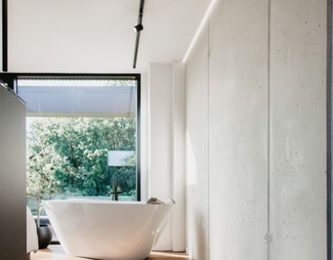 Modernes Badezimmer mit freistehender weißer Badewanne, großem Fenster mit Blick ins Grüne und minimalistischer Einrichtung.