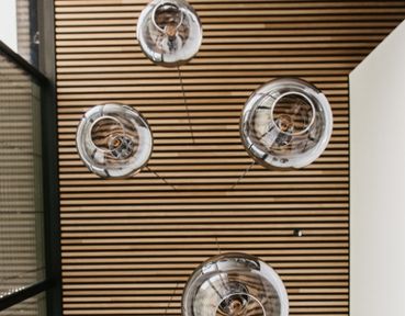 Fünf PANTILO Pendelleuchten mit Schirm aus Rauchglas, die von einer Decke aus Holzpanelen hängen, perspektivisch von unten betrachtet.