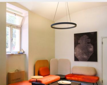 Moderner Raum mit bunten gepolsterten Sitzgelegenheiten, ONE CUBE Pendelleuchte, abstrakter Wandkunst und einem kleinen Fenster.