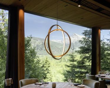 Esstisch mit eleganter Tischdekoration und ONE VERTICAL an einem großen Fenster mit Blick auf einen üppigen Wald und ferne Berge unter einem strahlend blauen Himmel.
