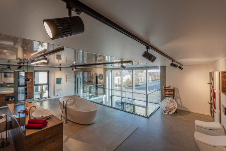 Modernes Badezimmer mit freistehender Badewanne, großen Spiegeln, Schienenbeleuchtung und Blick auf den Balkon durch Glastüren.
