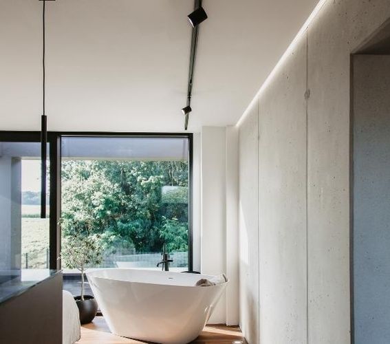 Modernes Badezimmer mit freistehender weißer Badewanne, großem Fenster mit Blick ins Grüne und minimalistischer Einrichtung.