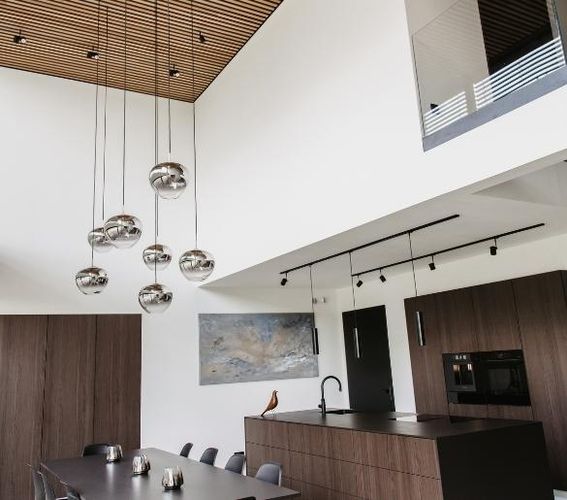 Moderner Essbereich mit hoher Decke, eleganten schwarzen Stühlen, Holzakzenten und hängenden Glaskugelleuchten (PANTILO). Minimalistisches und großzügiges Design.
