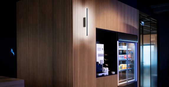 Ein moderner Verkaufsautomat mit beleuchteten Regalen in einem holzgetäfelten Gehäuse, in dem verschiedene Snacks und Getränke angeboten werden, beleuchtet von der ONE LINEAR 70