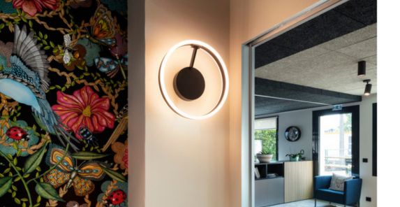 Ein modernes Interieur mit der ONE Wand- und Deckenleuchte, einem lebhaften Blumenwandbild und einem Blick in einen gemütlichen Wohnbereich mit natürlichem Licht.
