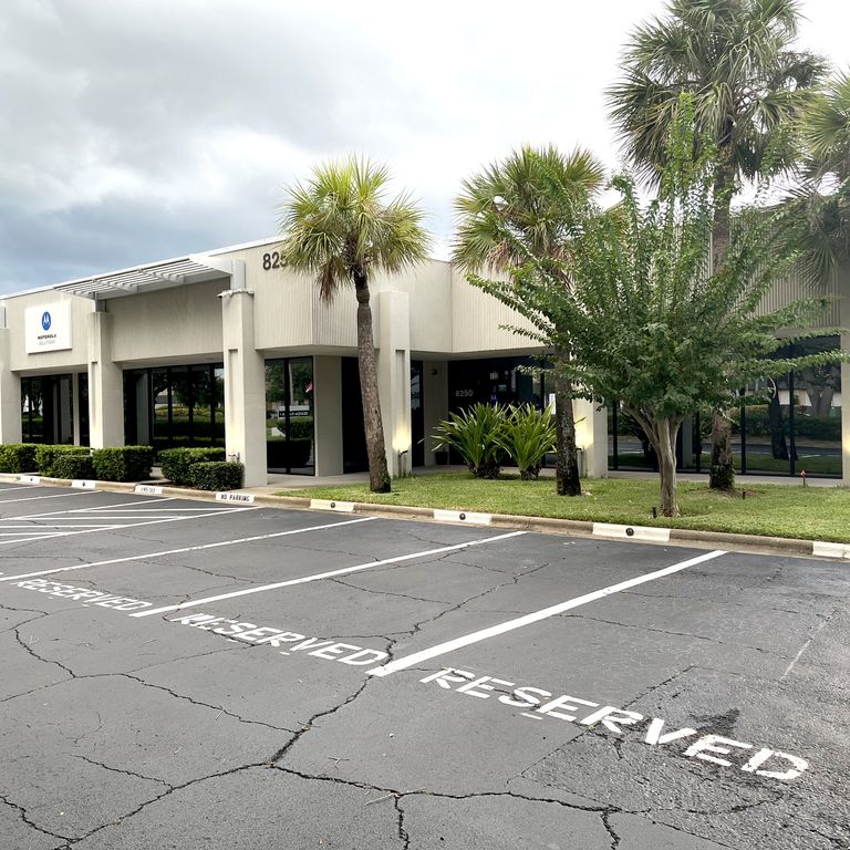 Office building with palm trees in front, reserved parking spaces, and a cloudy sky above.