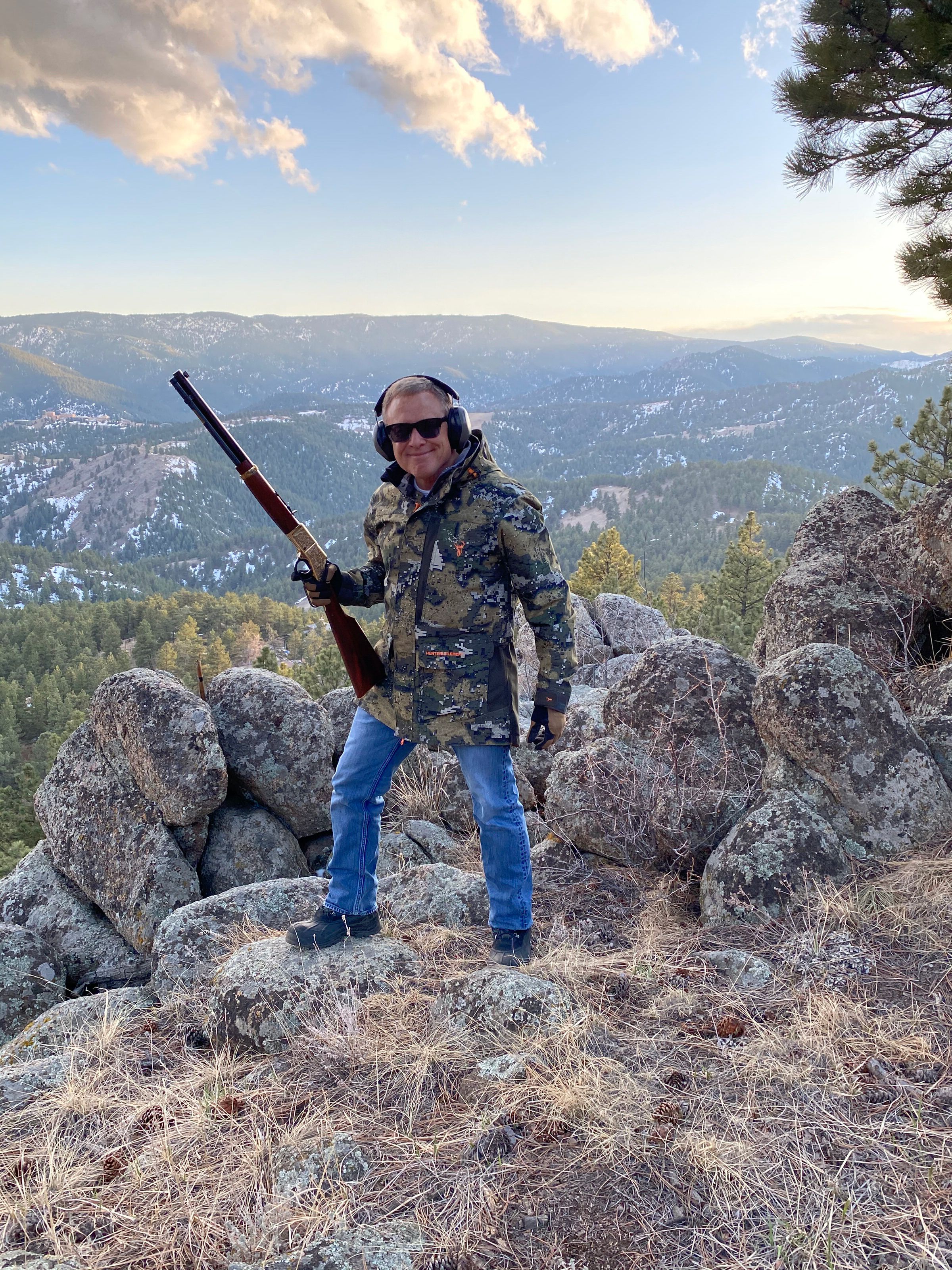 Brett Kingstone at the Max King Ranch standing on a rocky environment wearing hunting gear and holding a hunting rifle.