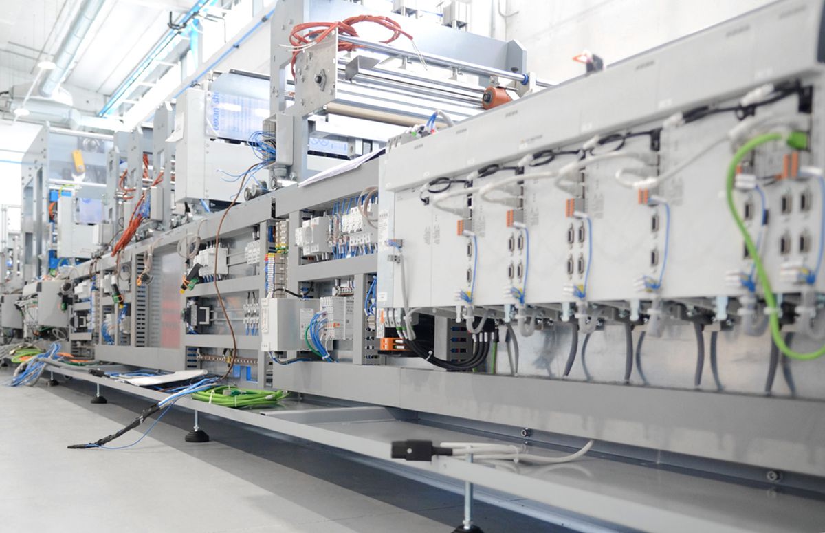 Seitenansicht einer industriellen Automatisierungsanlage mit offenliegenden Steuerungsmodulen, Verkabelung und Sensorik. Die präzise Struktur zeigt modernste Steuerungstechnik und Integration elektromechanischer Komponenten in der Produktion.