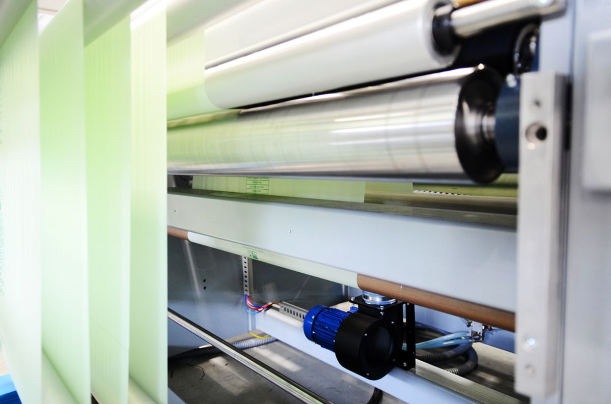 Detailansicht einer industriellen Walzenanlage mit laufenden Kunststoff- oder Papierbahnen. Sichtbar sind präzise gelagerte Rollen, Antriebseinheit und Führungen – Symbol für präzise Materialverarbeitung und automatisierte Steuerungstechnik.