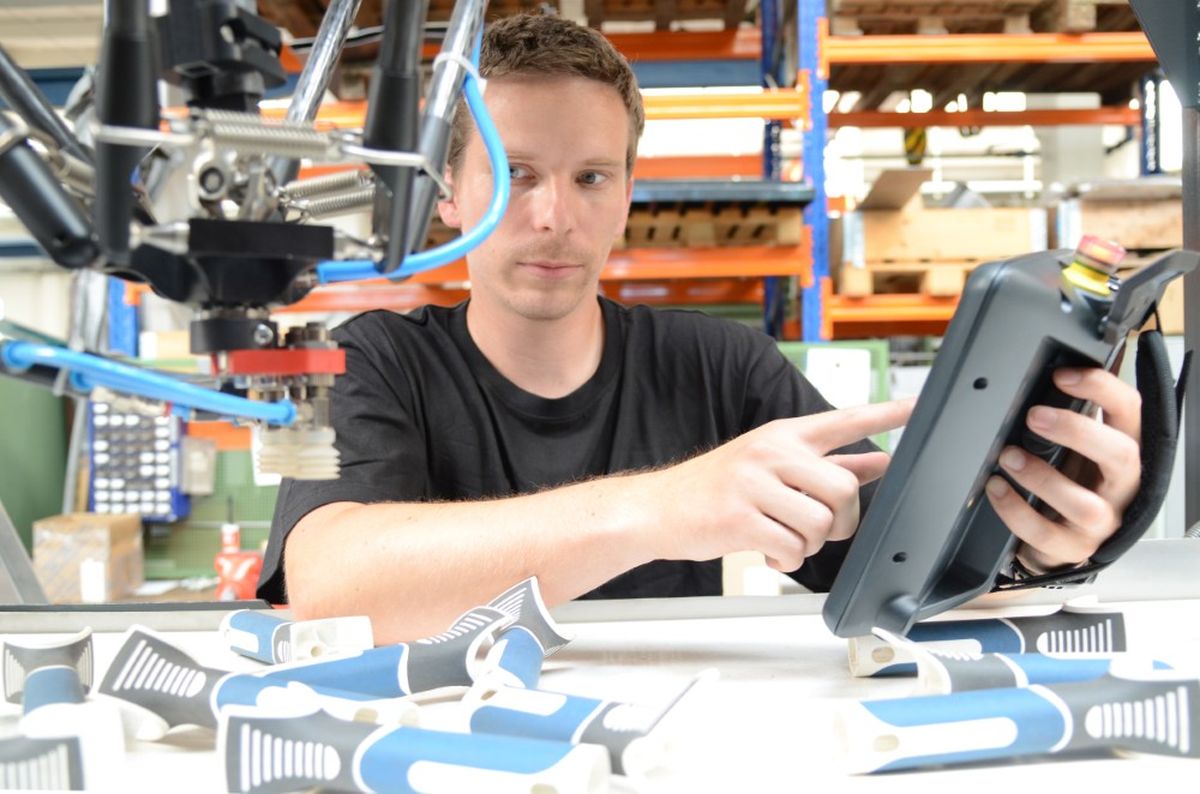 Jan Merkvart utilizza un HMI KEBA mobile all'interno di una cella robotizzata con un robot delta. I componenti in plastica vengono posizionati intorno a lui mentre controlla in modo sicuro le funzioni della macchina.