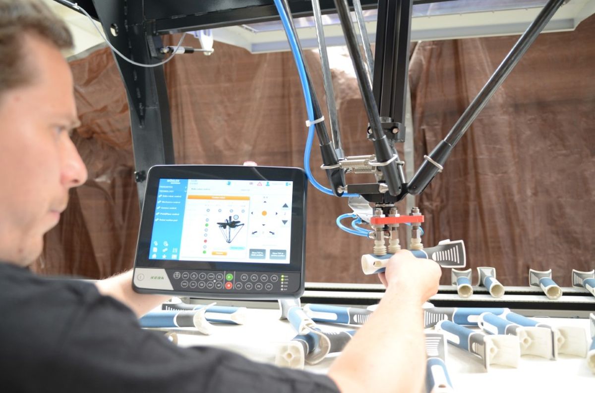 Un operatore programma un robot delta utilizzando un HMI KEBA KeTop Safe Wireless. Il display mostra le funzioni di controllo e visualizzazione per la messa in servizio sicura della cella robotizzata.