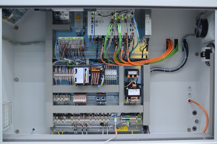 Innenansicht eines elektrischen Schaltschranks mit verschiedenen farbigen Kabeln, Steckverbindern und Bauteilen, die übersichtlich angeordnet und miteinander verbunden sind.