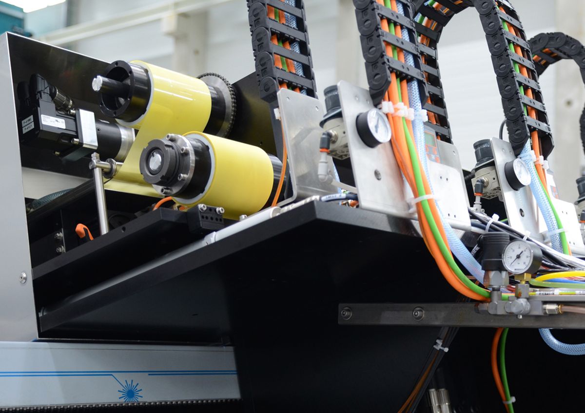 Nahaufnahme von Industriemaschinen mit gelben Walzen, bunten Kabeln und Metallkomponenten in einer Fabrikumgebung.