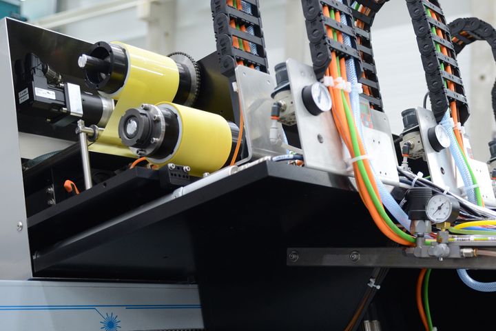 Nahaufnahme von Industriemaschinen mit gelben Walzen, bunten Kabeln und Metallkomponenten in einer Fabrikumgebung.