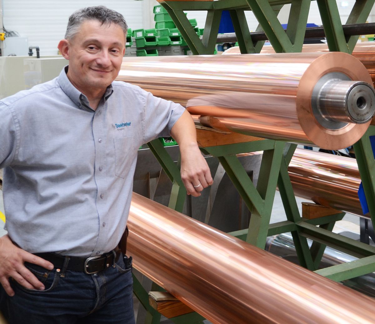 Hansjörg Michel, Head of Technology bei Daetwyler Graphics steht neben großen, glänzenden Kupferrollen auf einem grünen Industrieregal.
