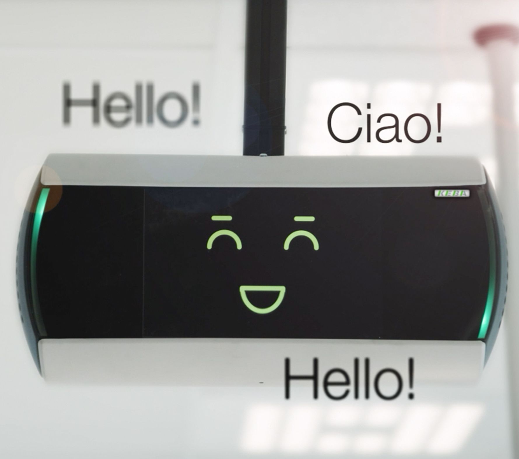 KeBob ist zu sehen – der digitale Bildschirm zeigt ein lächelndes Gesicht mit den Worten „Hello!“ und „Ciao!“, was eine freundliche Begrüßung in mehreren Sprachen suggeriert.