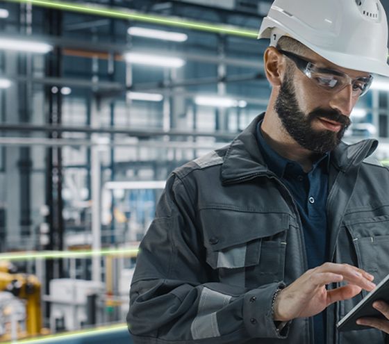 Engineer wearing a safety helmet working with a tablet in a modern industrial environment.