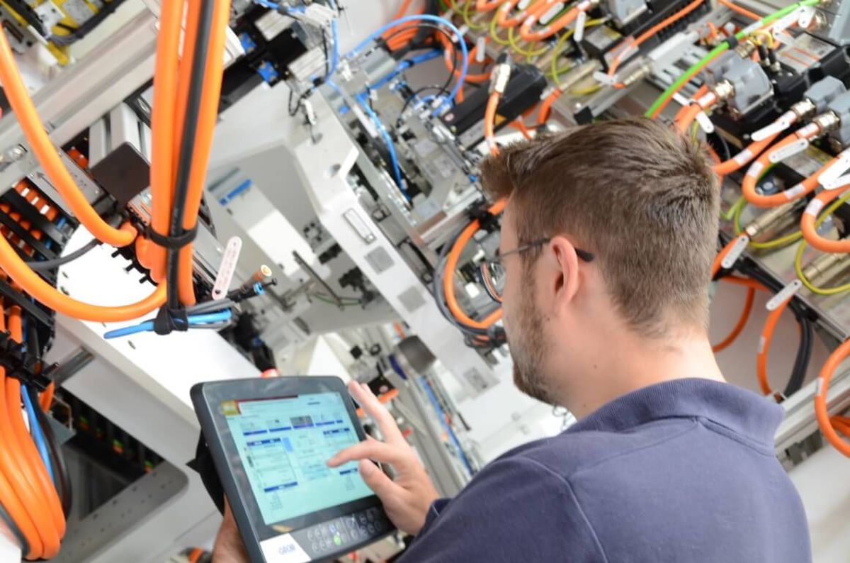 A technician operates a mobile control panel to manage a complex automation system with numerous orange cables and control components. The image represents precise machine control, connectivity, and modern industrial automation.