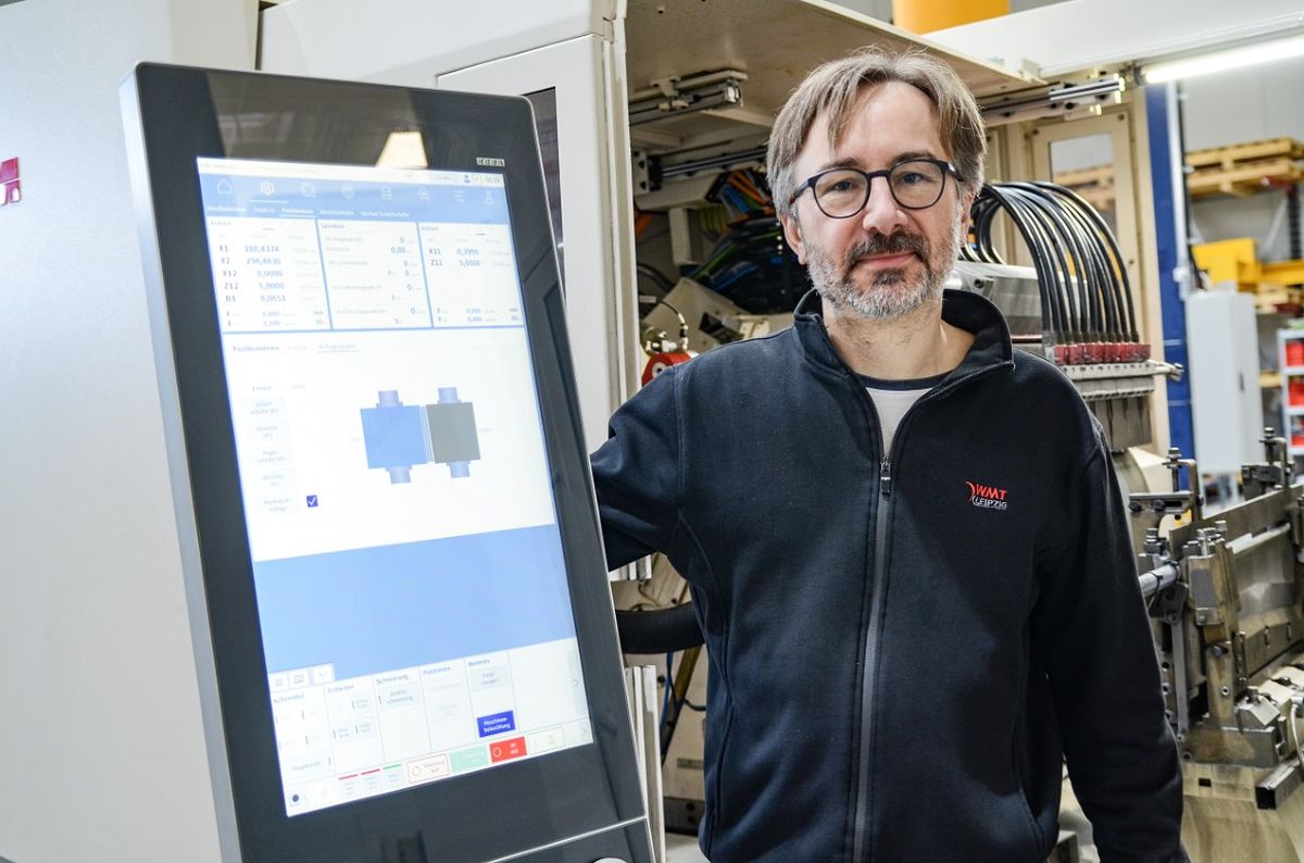 Stefan Cämmerer, Head of Software Development and Electrical Design, stands next to an HMI panel and looks at the camera, while a machine is visible in the background. The display shows graphical representations and process data.