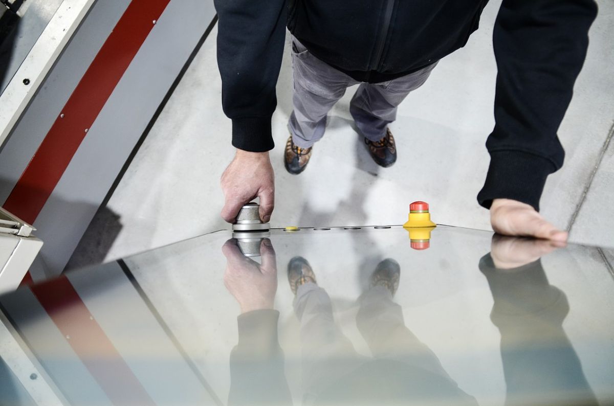 Person operating a machine with a control panel, using KeWheel near a red emergency stop button, viewed from above.